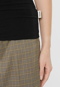 Schwarzes, figurbetontes Tanktop mit sichtbarem "SENSES"-Label an der Seite, kombiniert mit einem Hundehautmuster in Beigebräun und Blautönen.