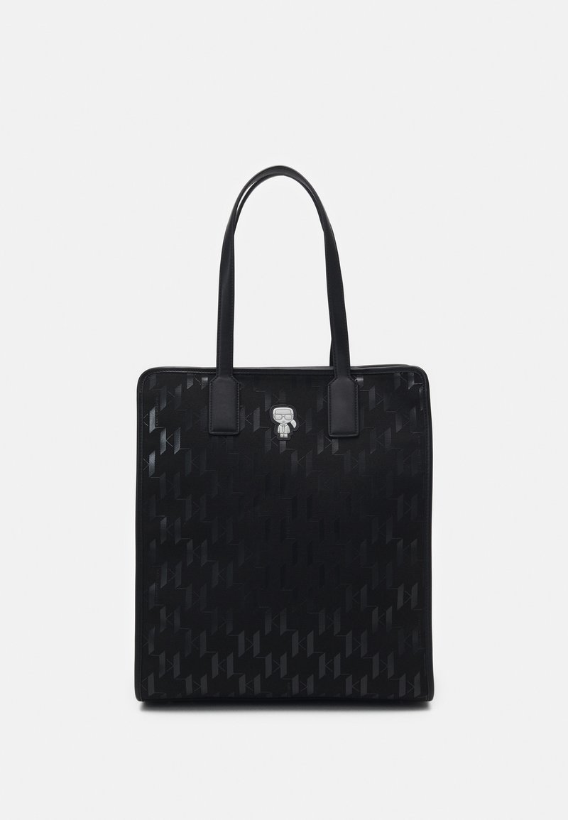 Sac cabas rectangulaire noir avec motif embossé subtil et petit emblème argenté de personnage de dessin animé sous les bretelles doubles.