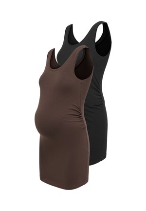Jeune femme enceinte portant une veste en cuir noire, un top noir, un jean bleu foncé et des mocassins noirs, debout avec une main dans la poche de la veste.