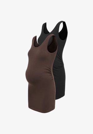 Jeune femme enceinte portant une veste en cuir noire, un top noir, un jean bleu foncé et des mocassins noirs, debout avec une main dans la poche de la veste.