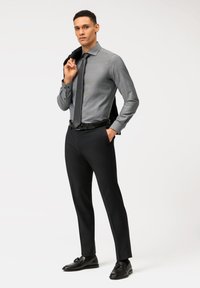Graues, strukturiertes Langarmhemd mit Kragen, kombiniert mit schwarzen, taillierten Hosen und Lederschuhen. Schwarzer Blazer über die linke Schulter drapiert.
