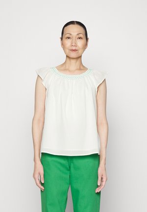 Top branco sem mangas com decote franzido, decorado com bordados em verde claro. O tecido é suave e fluido, combinado com calças verdes.