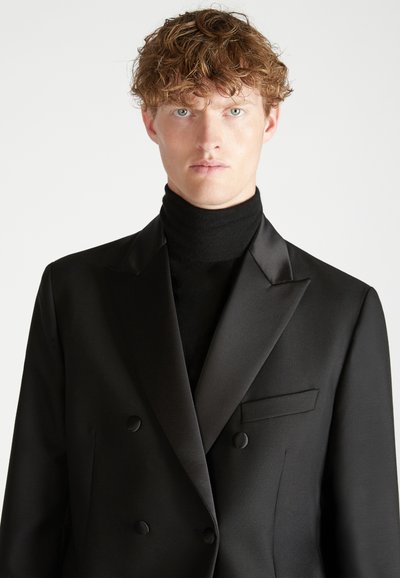 Zwarte dubbelgeknoopte blazer met satijnen afwerking, notch-lapels en een enkele pocket. Draagt over een zwarte coltrui.