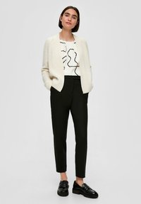 Crème rib gebreide cardigan, blouse met abstract patroon in het wit, zwarte op maat gemaakte broek en zwarte loafers, met strakke lijnen en gestructureerde pasvorm.