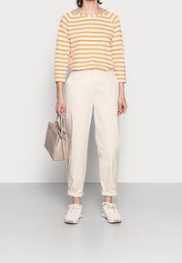Gestreiftes orange-weißes Langarmoberteil, cremefarbene tapered Hose, helle Sneakers und eine beige Handtasche. Einfaches Design und lässige Passform.