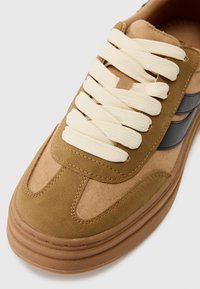 Brune semelskinn sneaker med teksturert overflate, utstyrt med kremfargede snørebånd, et grått aksent og en tykk gummisåle for bedre grep.