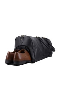 Schwarze Lederreisetasche mit einem Seitenfach, teilweise geöffnet, mit einem Paar brauner formeller Schuhe mit schwarzen Sohlen.
