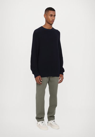 Pull en tricot navy à manches longues, col rond et poignets côtelés ; associé à un pantalon vert clair et des baskets blanches.