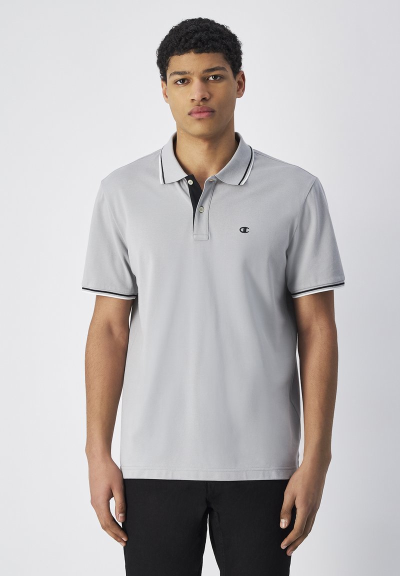 Graues Polohemd mit kontrastierendem schwarzen Kragen und Ärmelschlitzen. Kurze Ärmel, Material aus Baumwollmischung und ein kleines Logo auf der Brust.