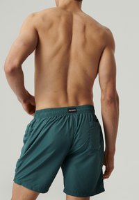 Turkusowe kąpielówki z lekkiego materiału, z elastycznym pasem, bocznymi kieszeniami i tylną kieszenią z małą metką z logo.