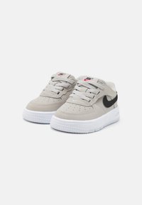 Nike sportcipők világosszürke velúr felső résszel, fekete swoosh-sal, fehér gumis középtalppal és csillagmintás, érdes felületű talppal.