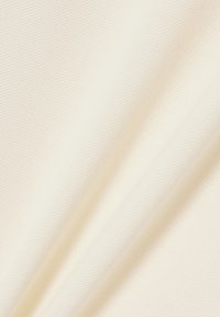 Lyse cremefarvet stof med en glat, let tekstureret overflade. Materialet har diagonale vævemønstre og falder blødt.