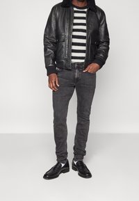 Svart läderbomberjacka med shearlingkrage, randig stickad tröja, grå slim-fit jeans och svarta slip-on skor.