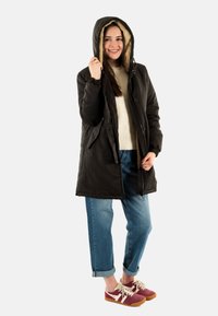 Chaqueta exterior negra con capucha, con un suave forro beige, jeans azules casuales y zapatillas burdeos con acentos beige.