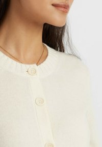 Cardigan lavorato a maglia color crema con un collo a costine, dotato di due bottoni rotondi e una texture morbida. Vista ravvicinata che mette in risalto il dettaglio dei bottoni.