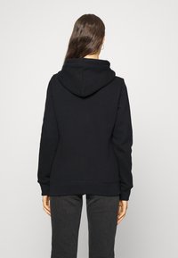 Sudadera con capucha negra hecha de un material suave, con un corte holgado, puños de canalé y un bolsillo tipo canguro en la parte frontal.
