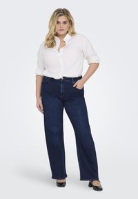 Dark blue high-waisted jeans with a straight leg fit, paired with a white button-up shirt and black flats. Smooth denim texture.