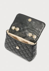 Μαύρη καπιτονέ τσάντα χειρός από δερματίνη με χρυσό κούμπωμα και δύο στρογγυλά κλειδώματα στο εσωτερικό· επενδεδυμένη με μπεζ ύφασμα.