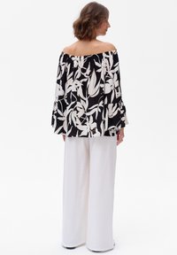 Bluzka na ramiączkach z czarno-białym kwiatowym wzorem, z zebranym dekoltem i szerokimi rękawami, w połączeniu z białymi szerokimi spodniami.