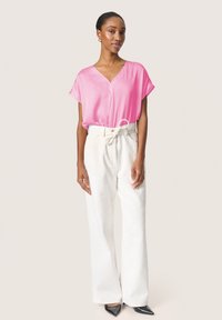 Blusa rosa de manga corta con diseño de escote en V, combinada con pantalones anchos blancos texturizados. Modelo llevando tacones negros de punta.