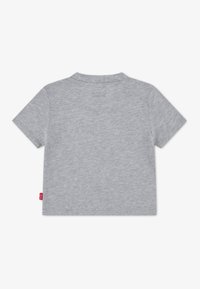 Γκρι μπλουζάκι με κοντά μανίκια κατασκευασμένο από μαλακό βαμβάκι, με στρογγυλή λαιμόκοψη και μια μικρή κόκκινη ετικέτα στη ραφή στο πλευρό. Λείο υφή, απλός σχεδιασμός.