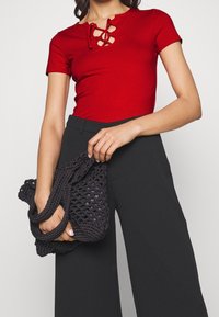 Top corto rojo de manga corta con detalle de cordones, combinado con pantalones negros de talle alto. Bolsa de croché negra sostenida en la mano, mostrando un diseño texturizado.