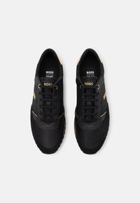 Svarta sneakers med guldaccent, ovandel i mocka och textil, rund tå, snörning och vadderade sulor för komfort.