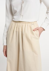 Béžová, lehká sukni z látky s elastickým pasem, volným střihem a boční kapsou. Doplněná bílou košilí s knoflíky.