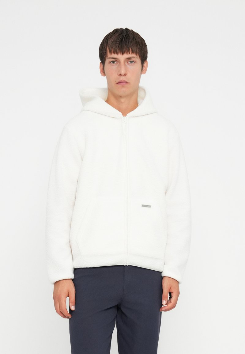 White fleece hoodie with a zipper and two front pockets. Features a soft texture and a small silver tag on the front.