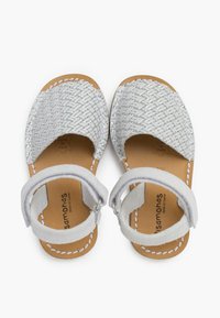 Geweven zilveren leren sandalen met een tan kleuren zool, open-teen ontwerp, verstelbare enkelband en witte stikdetails.