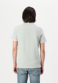 Polo-shirt à manches courtes vert clair avec des bordures contrastantes autour du col et des manches ; tissu doux, design simple et coupe ajustée.