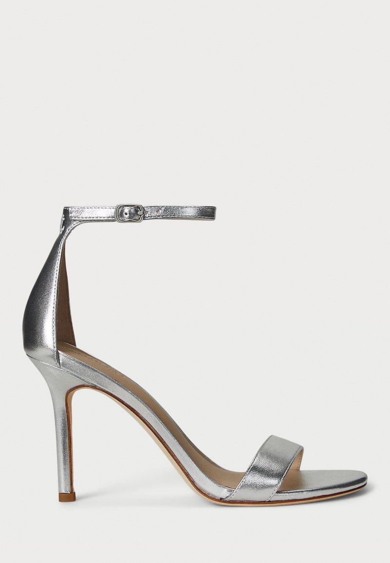 Sandalha de salto alto prateada com uma tira estreita nos dedos, tira no tornozelo com fecho de fivela, design elegante e textura metálica suave.