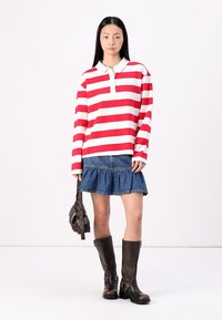 Chemise polo à rayures rouge et blanche à manches longues, jupe en denim à volants, bottes en cuir marron montantes jusqu'aux genoux, petit sac à bandoulière noir.
