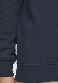 Navy blue sweatshirt with ribbed cuffs and hem. Fabric appears soft with a subtle texture. Small label visible on the side seam.