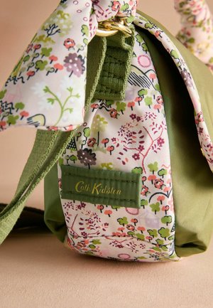 Groene stoffen tas met een bloemmotief panel. Voorzien van een gouden ring en een groen label met "Cath Kidston" in gouden letters.