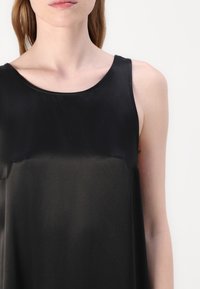 Top negru fără mâneci, cu o textură netedă și lucioasă și un guler rotund. Fără modele sau accesorii vizibile, având un design simplu.
