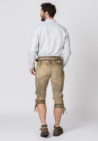 Braune Leder-Shorts mit aufgerollten Säumen und Bändern, kombiniert mit einem hellgrauen Hemd mit Knöpfen. Die Schuhe sind braun mit einem grünen gestrickten Akzent.