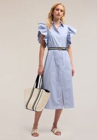 Rochie cămașă în dungi bleu deschis, cu mâneci fluturate, talie cu brățară și închidere cu nasturi în față. Asortată cu o geantă de umăr crem și sandale.