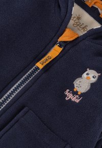 Marineblaue Fleecejacke mit Reißverschluss, orangefarbigen Akzenten und einem gestickten Eulendesign neben dem Markennamen "Sigikid."