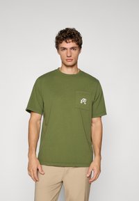 Olive green cotton t-shirt with short sleeves, a round neckline, and a chest pocket featuring a white logo design. Smooth texture.