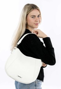 White leather handbag with a curved shape, adjustable strap, and metal hardware. Textured surface, label at the bottom, worn on shoulder.