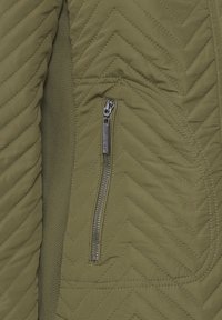 Veste matelassée vert olive avec une poche zippée, présentant un motif en chevron, une texture lisse et des panneaux latéraux élastiques.