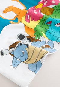 Tre creature colorate dei cartoni animati: drago arancione, tartaruga blu con cannoni e rettile blu con foglie verdi su tessuto bianco.