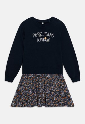 Námořnicky modré svetrové šaty s dlouhými rukávy; vršek zdobí nápis „PEPE JEANS LONDON“ v bílé barvě. Sukně je květinově vzorovaná v oranžové, modré a bílé barvě.