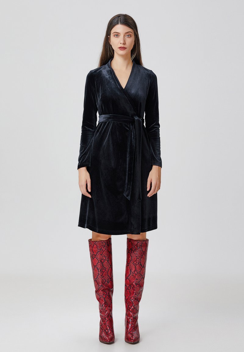 Robe enveloppante en velours noir avec des manches longues et une taille à nouer, accompagnée de bottes rouges à motif serpent montantes jusqu'aux genoux. Texture lisse et forme structurée.