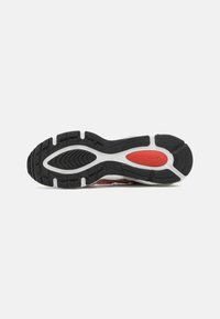 Semelle de chaussure avec motif de bande de roulement noir et blanc et un détail ovale rouge dans la zone de la voûte plantaire, sur un fond clair uni.