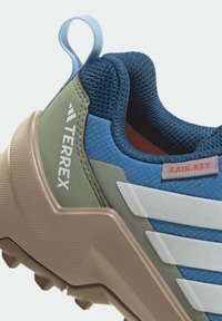 Περίπατος παπούτσι Terrex εξωτερικού χώρου σε μπλε, πράσινο και μπεζ. Διαθέτει επάνω μέρος από υφαντό υλικό με υφή, λευκές ρίγες και θηλιά για τράβηγμα. Ελαστική σόλα με εξογκώματα για πρόσφυση.