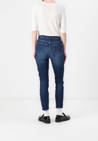 Jeans ajustados de denim azul oscuro con bolsillos traseros, combinados con una blusa blanca de manga corta y mocasines negros. Diseño simple y ceñido.
