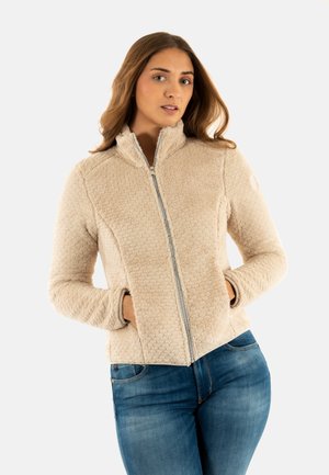 Giacca in pile beige con un motivo testurizzato, colletto alto, chiusura frontale con zip e tasche laterali, abbinata a jeans blu.