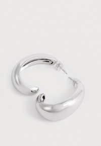 Para masywnych, błyszczących srebrnych kolczyków w kształcie półksiężyca z przezroczystymi plastikowymi zapięciami na białej powierzchni.